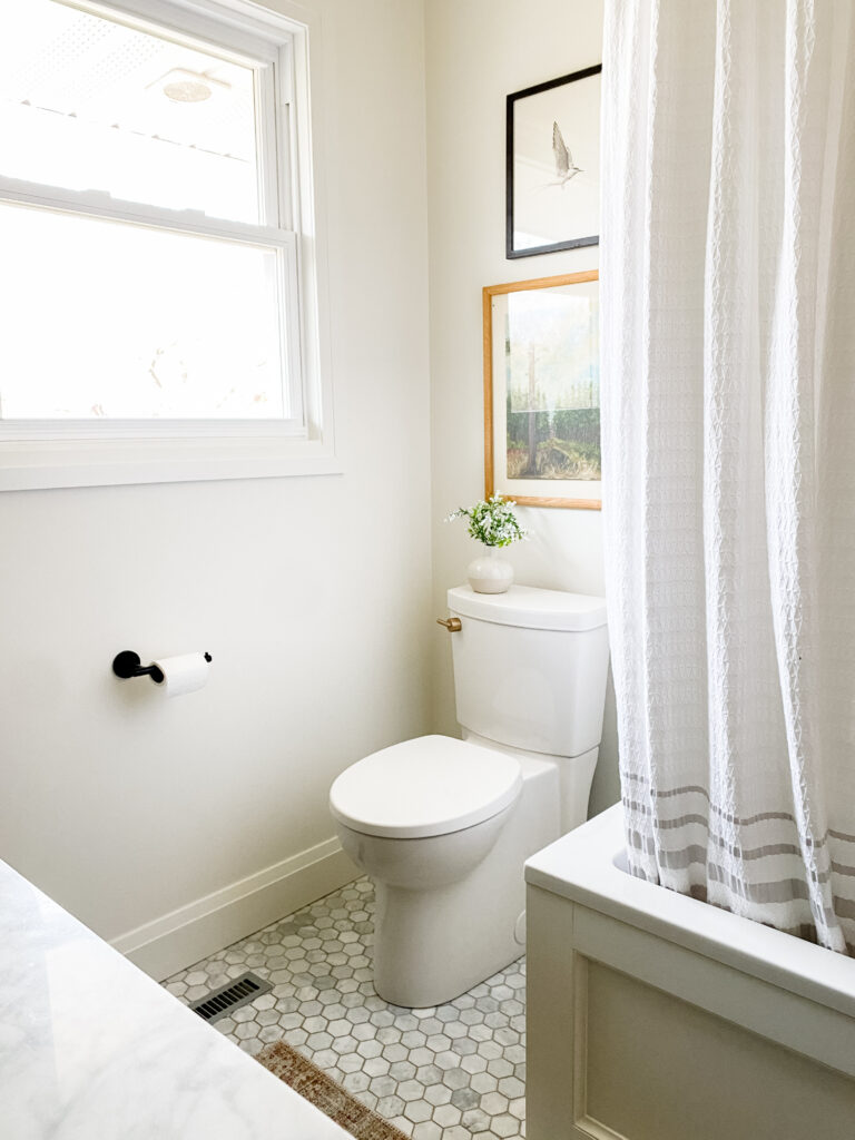 Clean line toilet with art above it next to a bathtub.