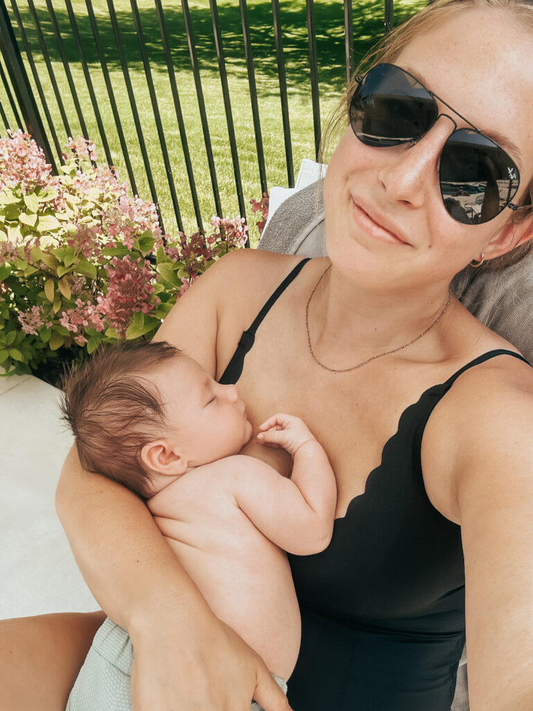 Happy woman wearing sunglasses holding her baby by the pool on a sun lounger.